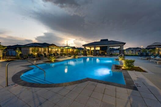 The pool area at dusk at our apartments for rent in Queen Creek, AZ, featuring beach chairs, umbrellas, and a clubhouse.