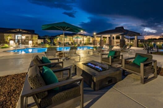 The pool area at our apartments in Queen Creek at twilight, featuring a fountain, beach chairs, and umbrellas with tables.