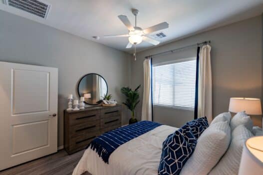 Model bedroom at our apartments for rent in Queen Creek, AZ, featuring wood grain floor paneling and windows with blinds.