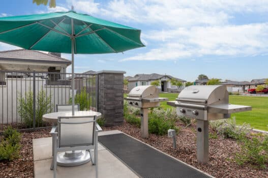 Outdoor lounge at our apartments in Queen Creek,featuring an umbrella, two grill stations, and a table with a chairs.